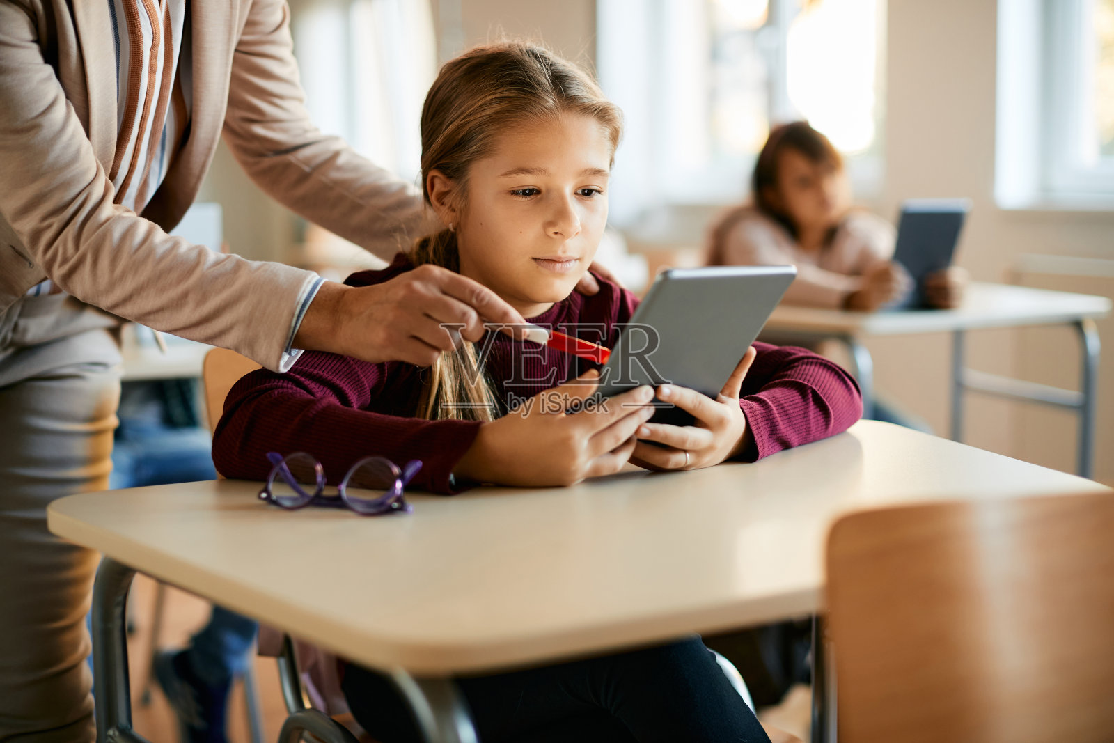 小女孩在老师的帮助下使用触控板在小学上课。照片摄影图片