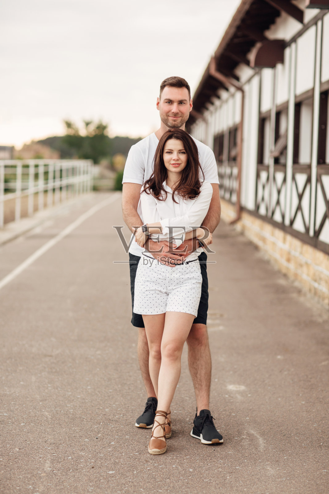 在一个温暖的夏日，快乐的年轻人和女人在户外玩耍。一对夫妇在马场附近拥抱照片摄影图片