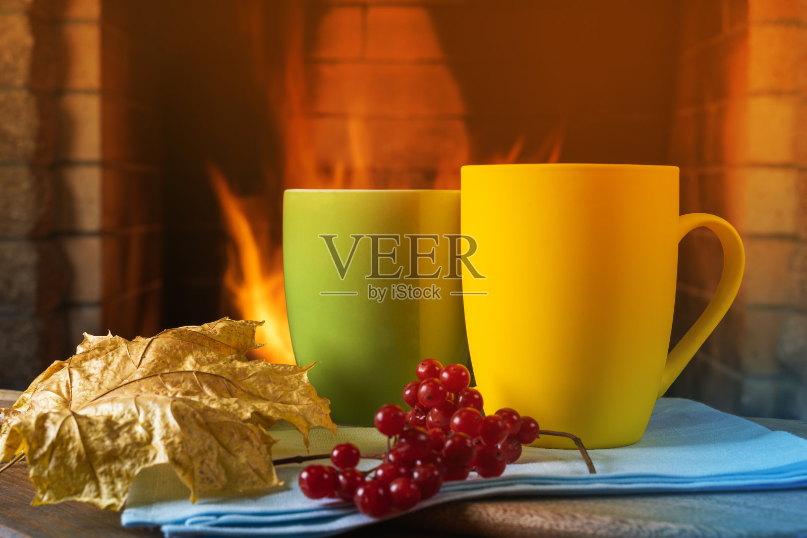 温暖的壁炉前放着热茶、浆果和秋叶的杯子。照片摄影图片