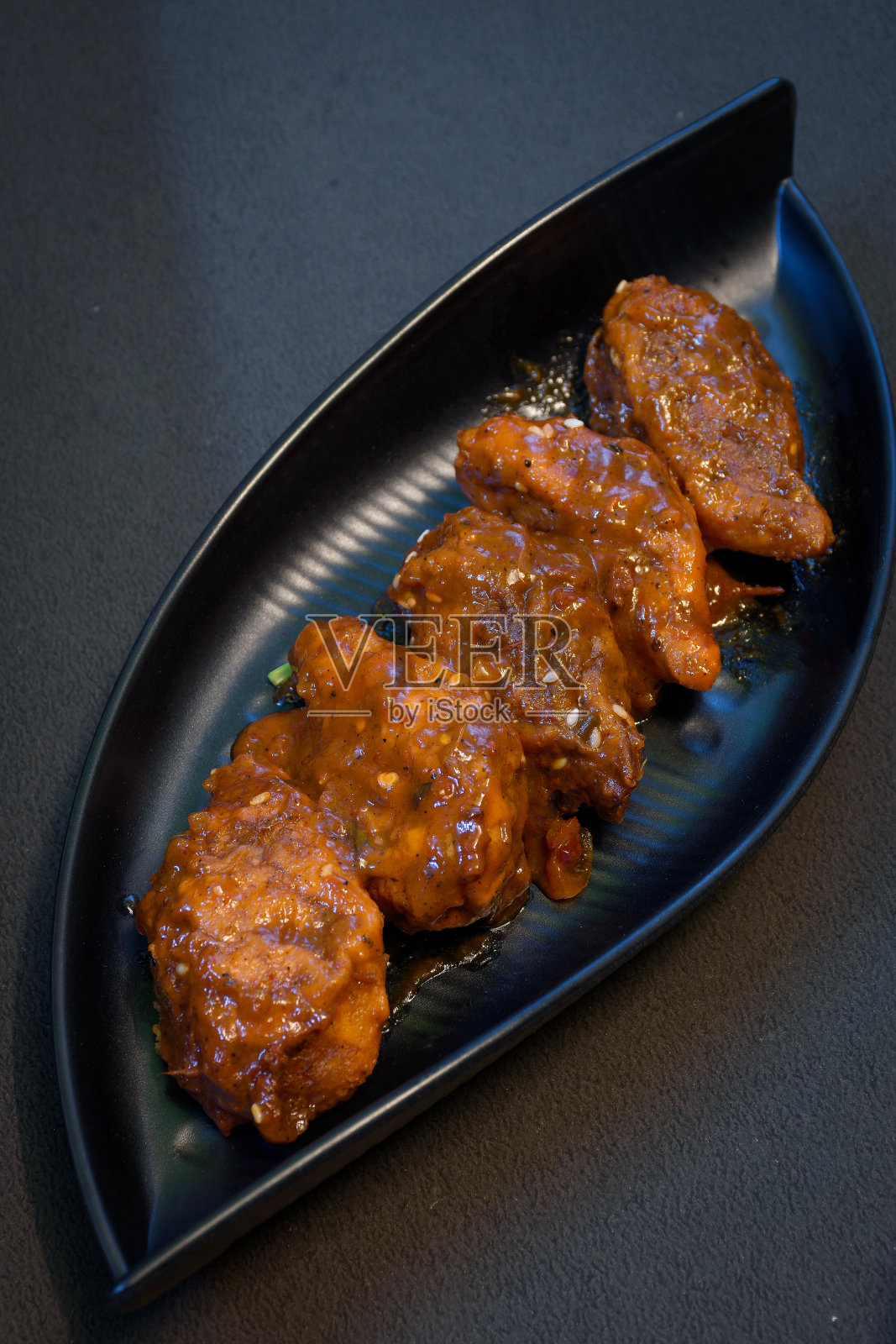 在黑色的背景上，用煎锅煎的鸡肉夹着酱汁，放在黑色的盘子里。照片摄影图片