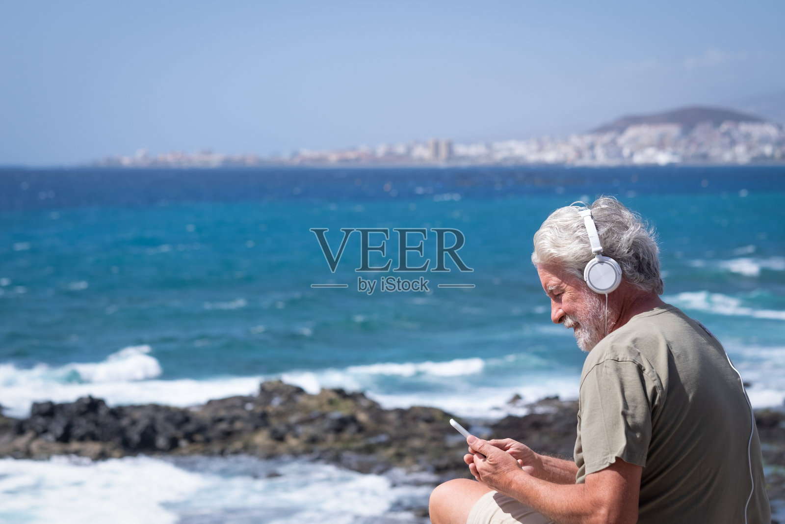 微笑的老人，胡子和白发，在大风天的海上使用电话。老年人享受假期和大自然的美照片摄影图片
