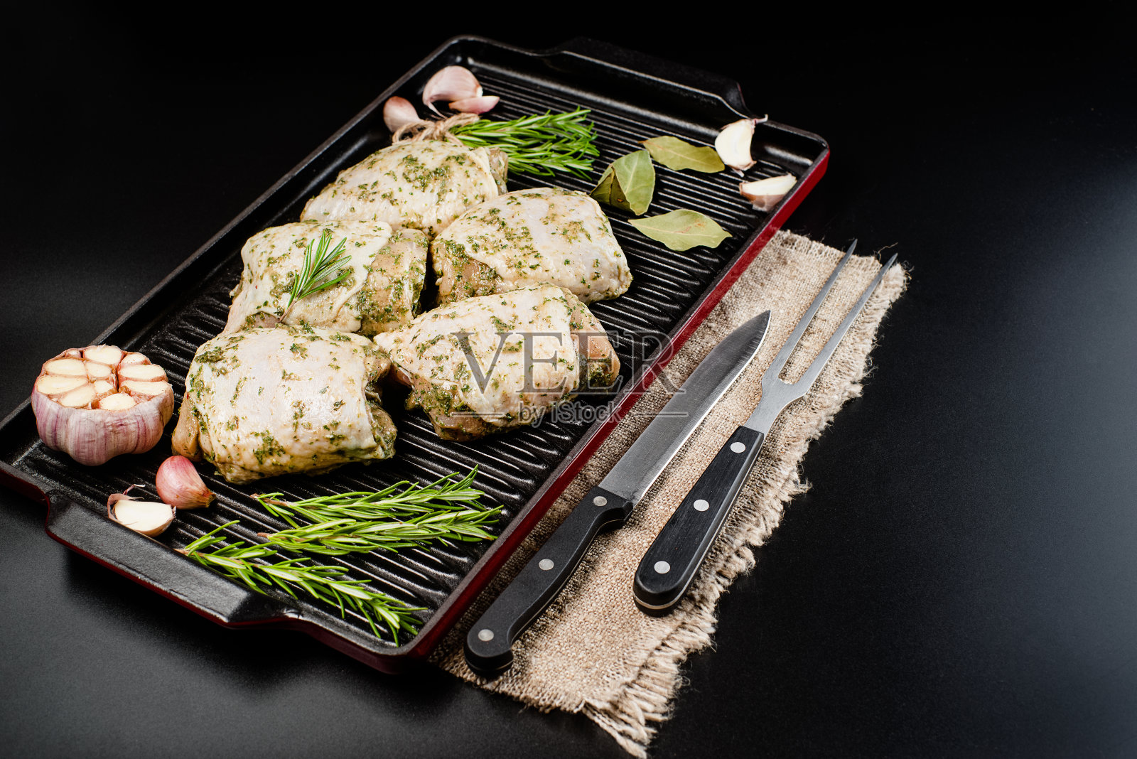 背景是腌过的生鸡腿，放在烤盘上，淋上清淡的香草酱。新鲜腌制的烤鸡。照片摄影图片