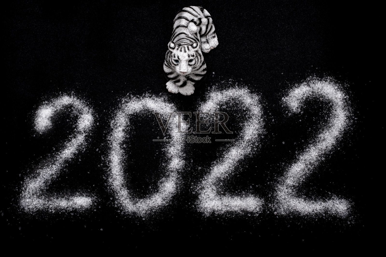 2022年新年快乐。2022年中国新年。玩具虎和2022年的日期写在像雪一样的盐，孤立在黑色的背景上插画图片素材