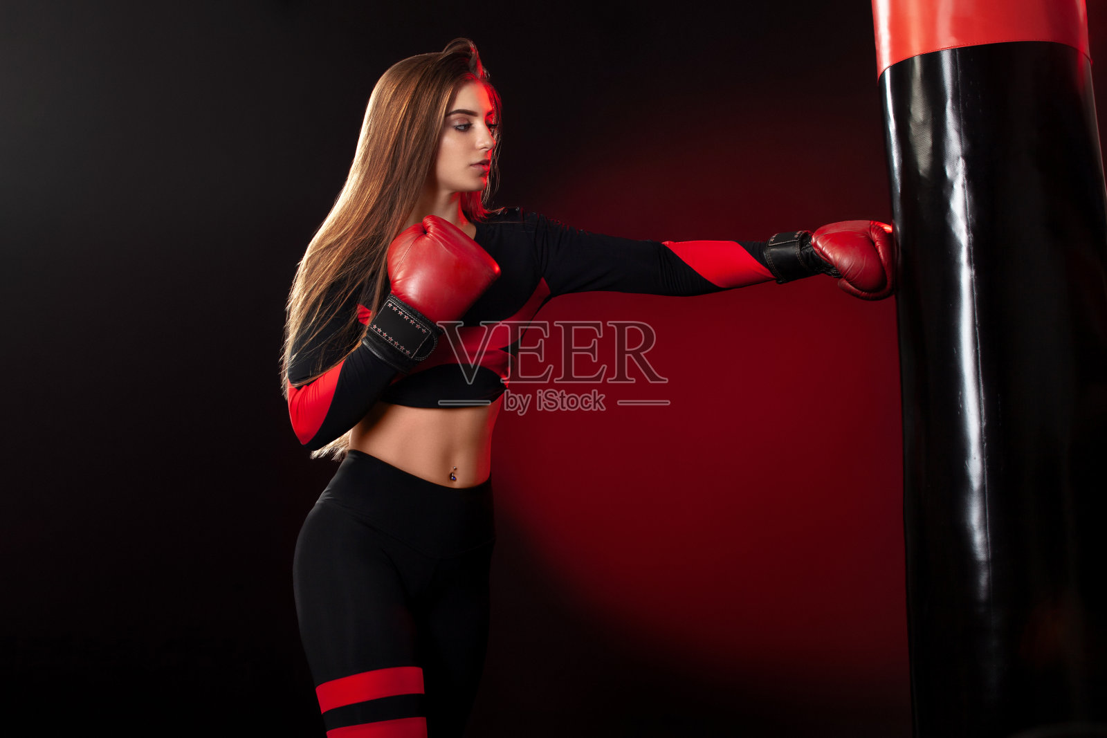 年轻的女运动员在体育馆里进行拳击训练。女孩戴着手套，穿着运动服，击打着拳击袋。孤立在黑色背景与烟雾。副本的空间。照片摄影图片