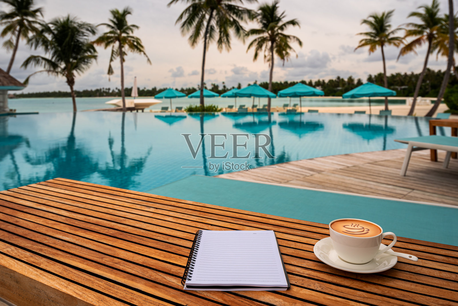 日落时分，游泳池旁边的木桌上放着笔记本和一杯咖啡照片摄影图片