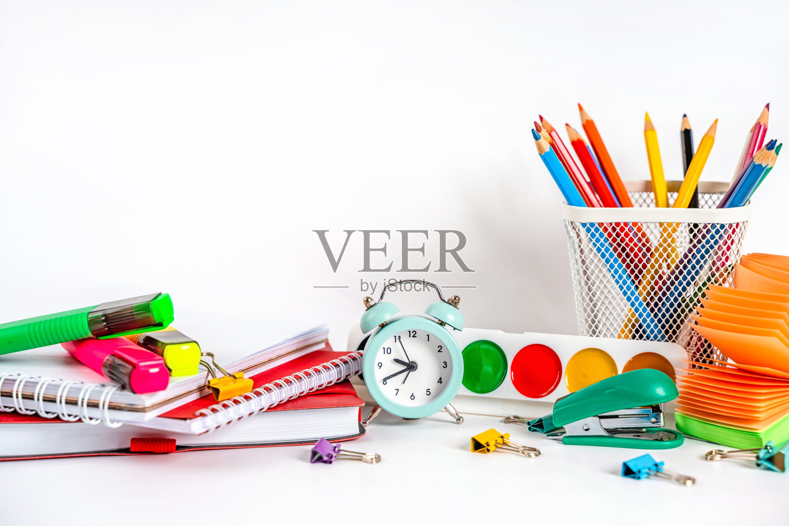 一张学校用的桌子，有彩色文具，油漆，白色背景上的闹钟。回到学校的概念。照片摄影图片