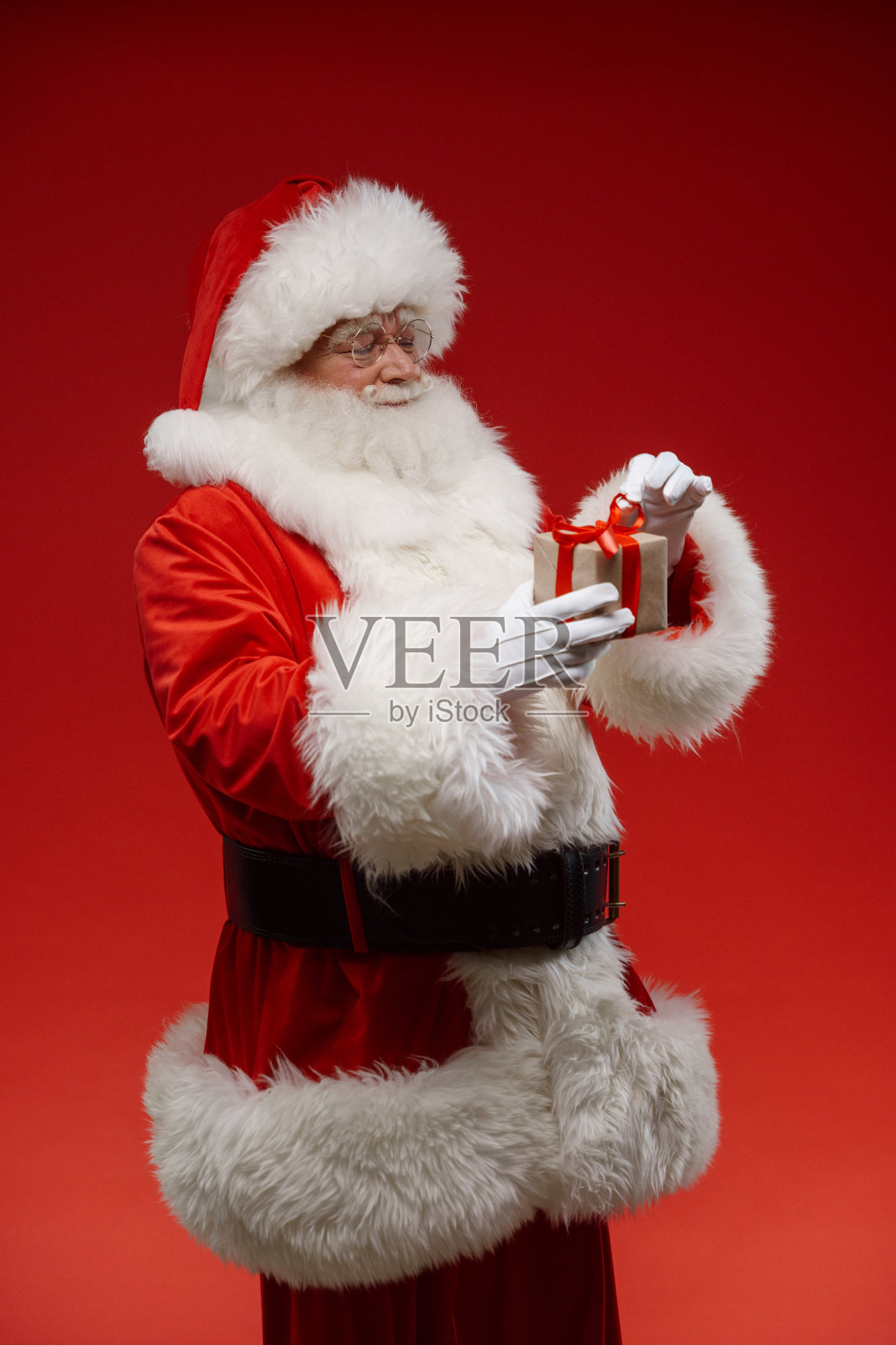 圣诞老人将要打开一个小礼品盒，站在一个专业演播室的红色背景上照片摄影图片