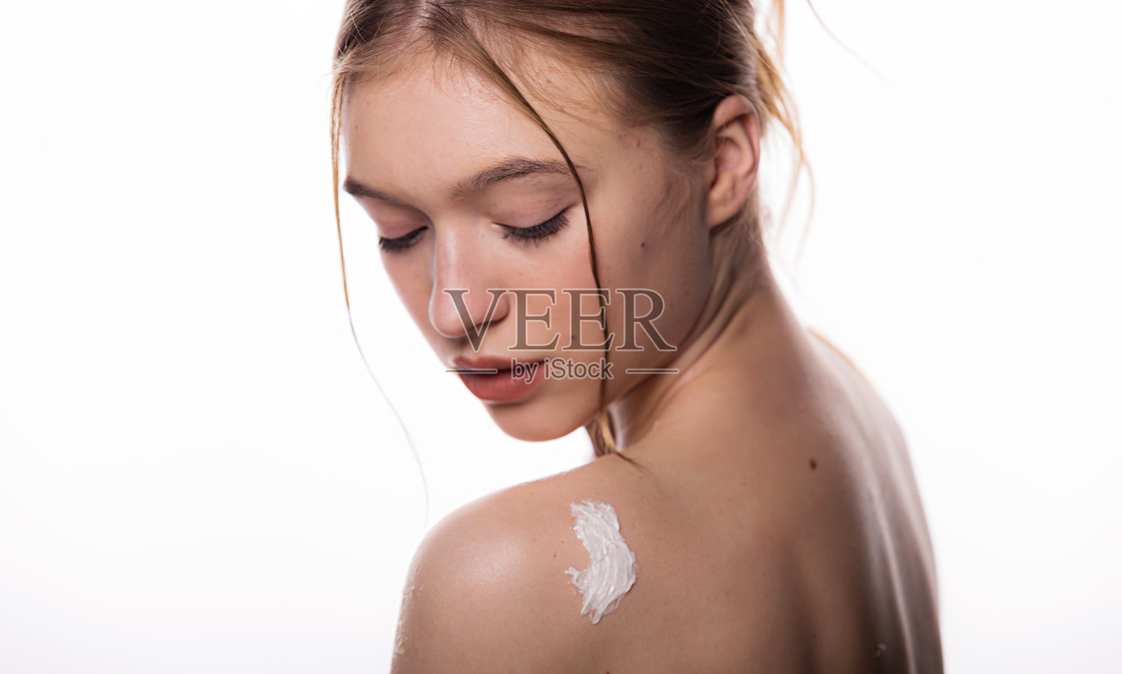 护肤女士把乳霜在她的身体上。年轻女子把药膏涂在肩胛骨上。隔离在白色背景，复制空间。保持年轻和美丽照片摄影图片