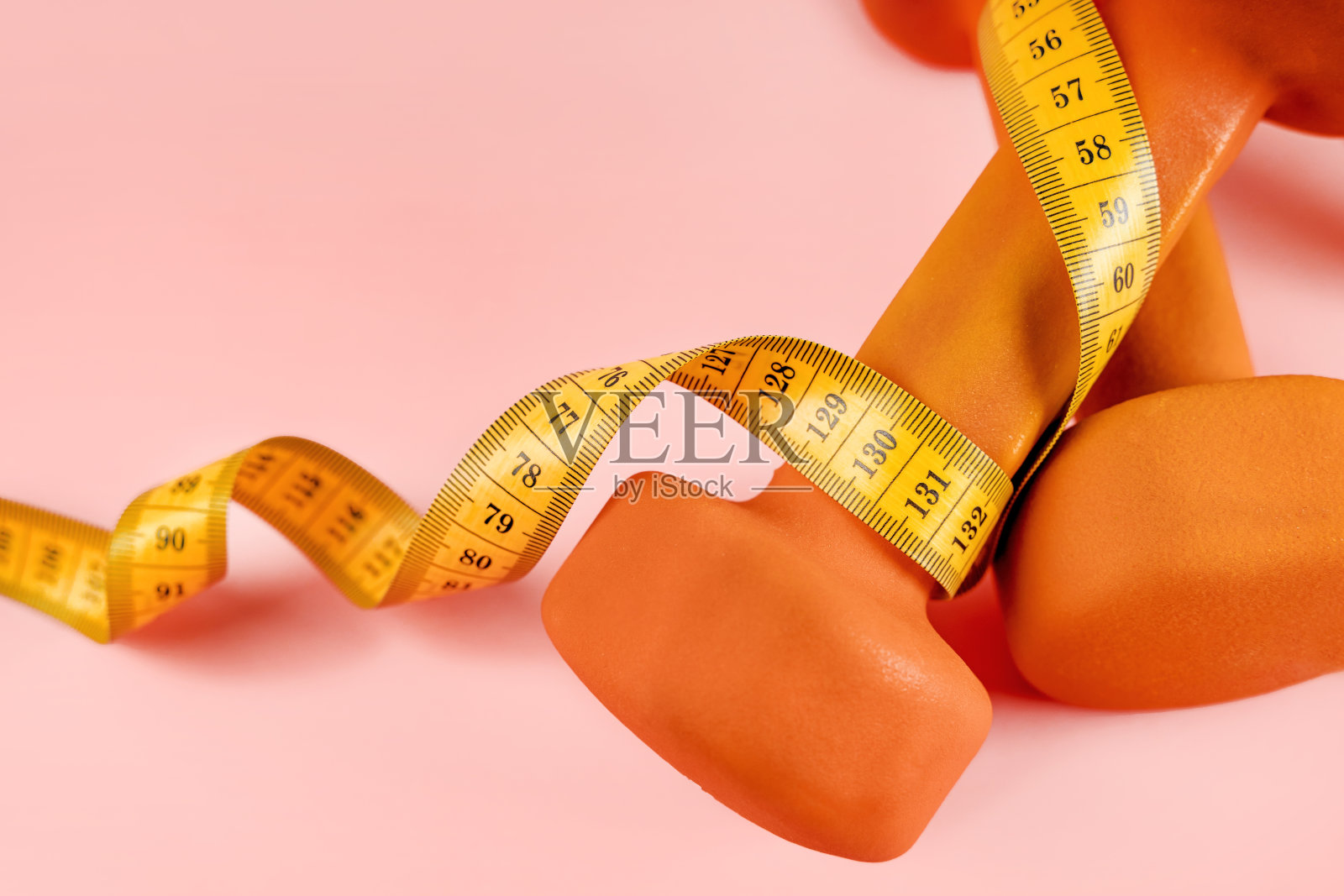 用黄色卷尺测量粉红色背景上的哑铃。运动、饮食和减肥的概念照片摄影图片