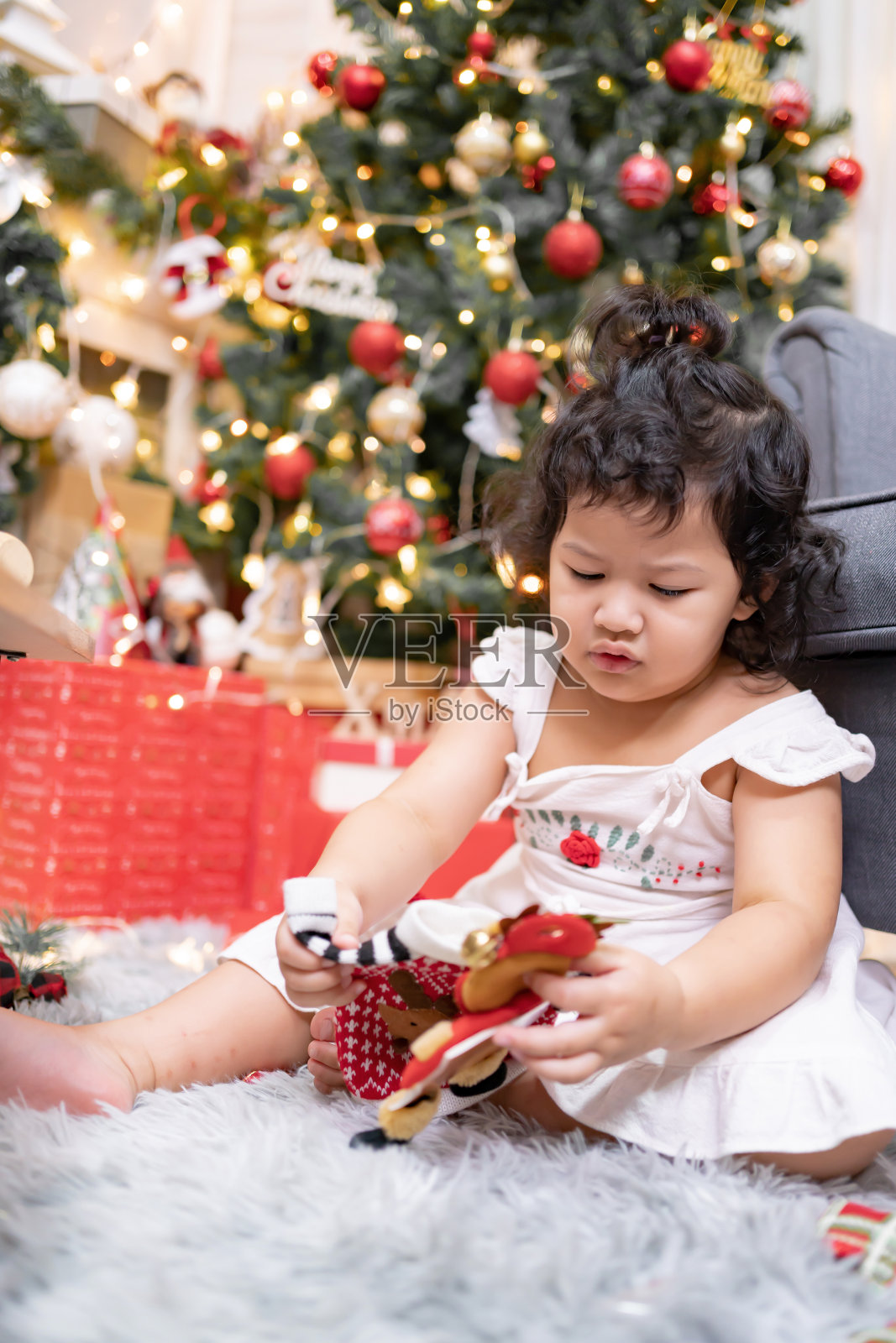 快乐的亚洲小女孩有乐趣在圣诞节。节日期间，孩子和父母在家里用圣诞树装饰。照片摄影图片