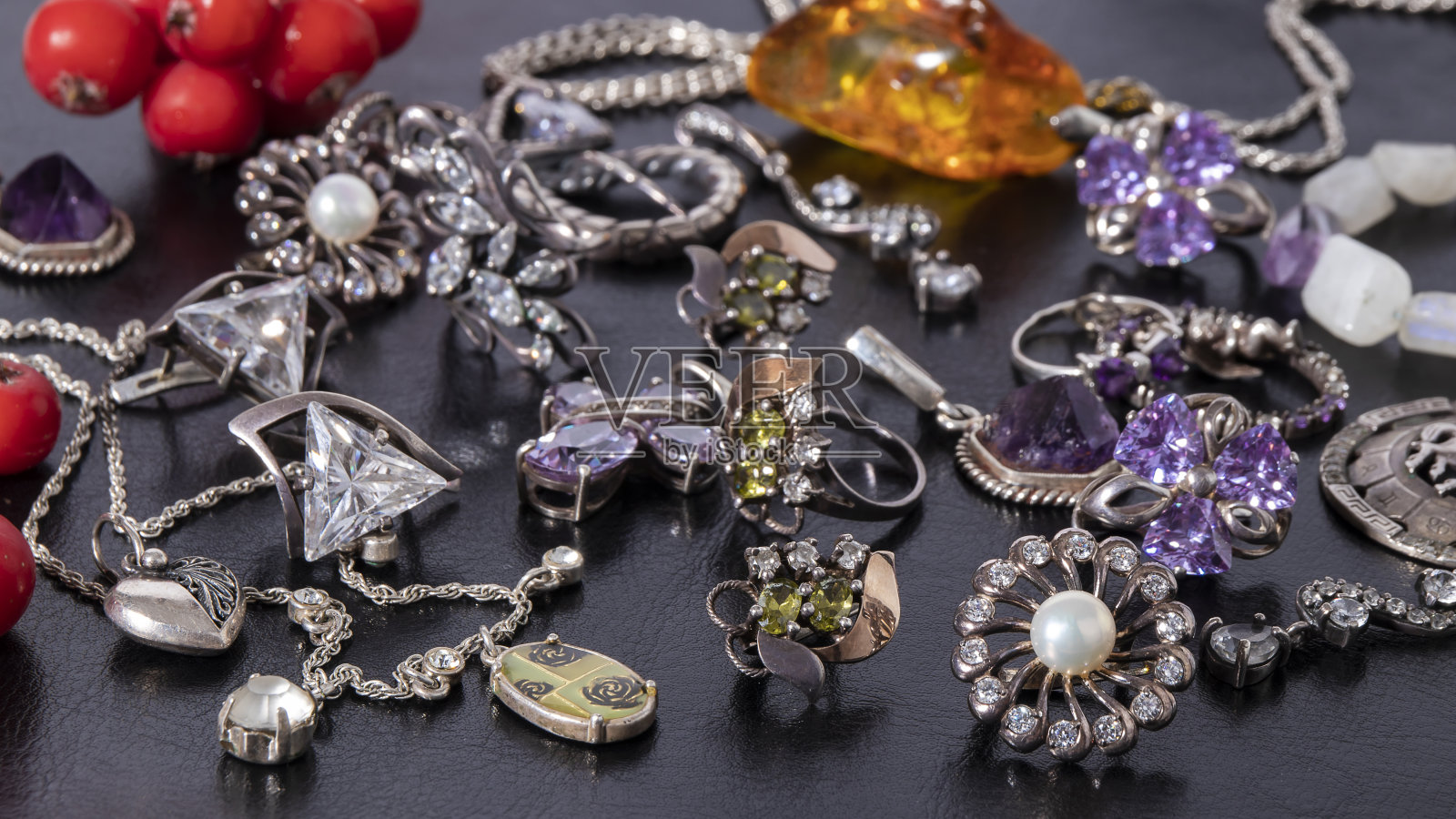 各种不同的银耳环，戒指，吊坠在黑色皮革的背景。镶有宝石的孤立的银首饰。照片摄影图片