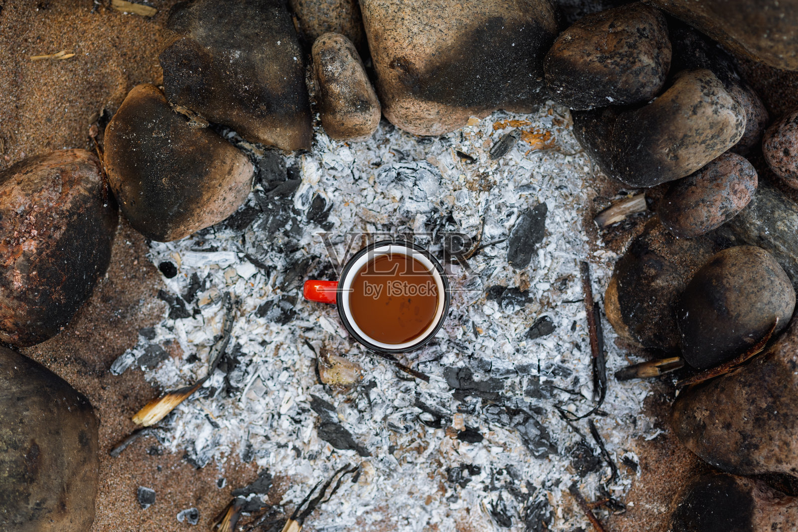 远足和户外活动，美丽的篝火和一杯红色的咖啡或茶。在海边或湖边有大石头的沙滩上野餐。露营生活和徒步旅行或荒野旅游照片摄影图片