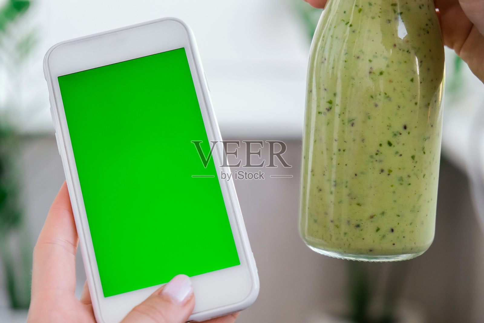 女人检查智能手机与色度键绿屏幕喝素食冰沙饮料排毒。在家里做瑜伽的女人。清洁饮食、减肥、健康饮食的饮食理念。保持健康照片摄影图片