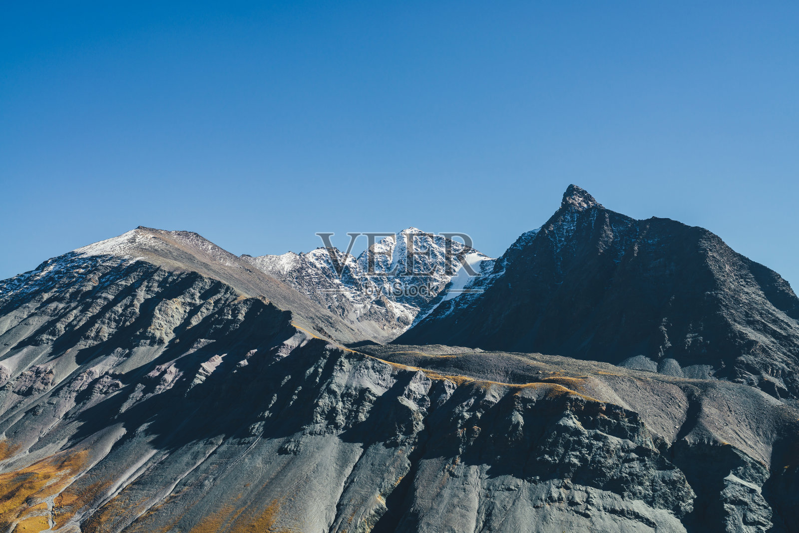 秋日阳光下，陡峭的石峰和白雪皑皑的高山风光。色彩斑斓的秋天景色，在蓝天下的阳光下，有灰色、黑色、橙色的山峰。照片摄影图片