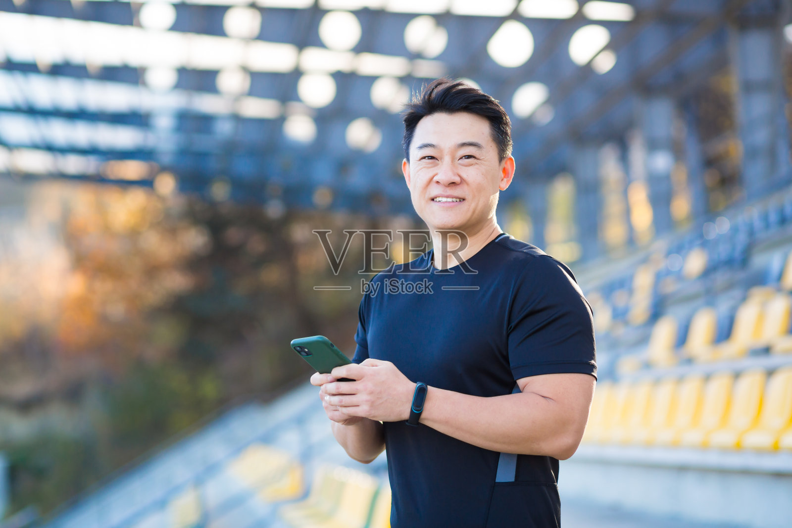 一名健康的男性在户外锻炼完后，用4g无线设备上的应用程序观看手机视频。亚洲运动员在跑步休息后开心地微笑着照片摄影图片