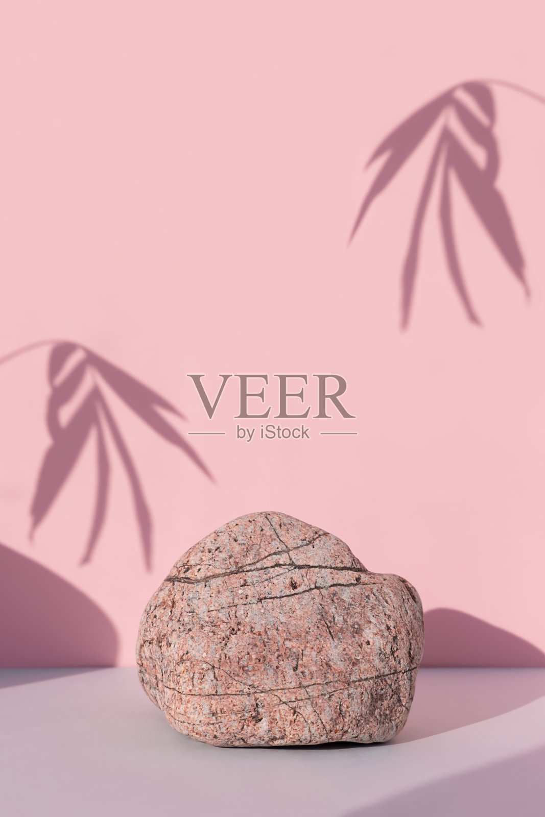 一个由石头做成的讲台放在灰色的桌子上，靠在粉红色的墙上，墙上有棕榈树叶的影子。照片摄影图片