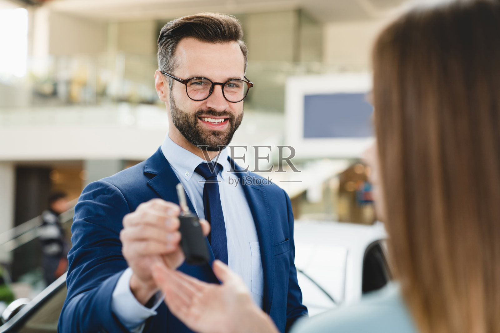 一个穿着正装的英俊白人男性店员在买完新车后给女顾客车钥匙的特写镜头。照片摄影图片