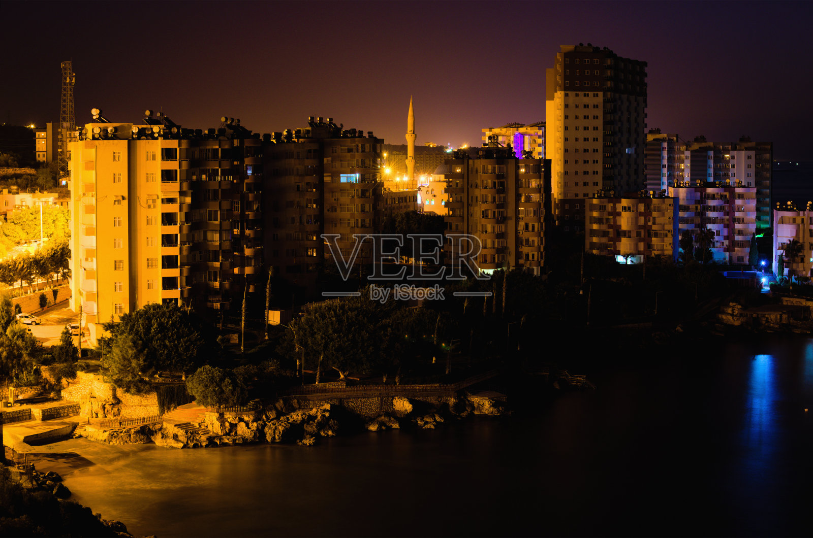 风景如画的夜晚灯光景观典型的土耳其小镇。土耳其梅尔辛附近地中海堤岸附近的住宅建筑。建筑物之间的清真寺高尖塔照片摄影图片