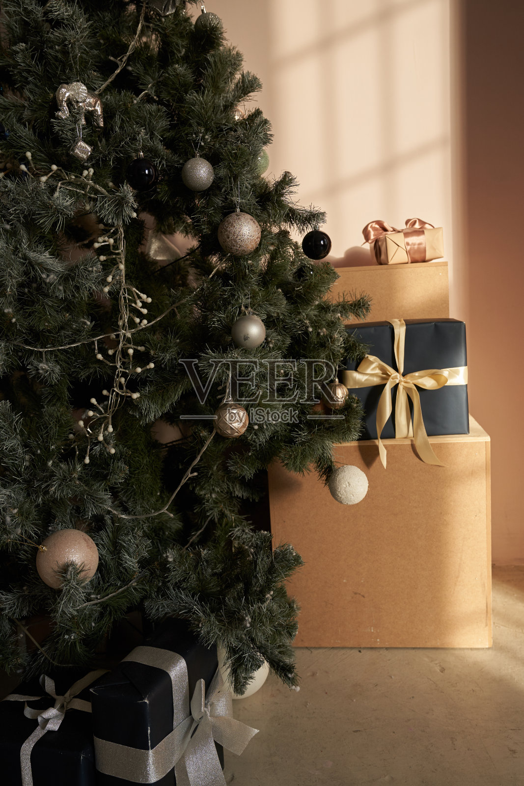 很多礼品盒是用米色纸和黑色做的，配上米色丝带。在圣诞树旁边的纸背景上照片摄影图片