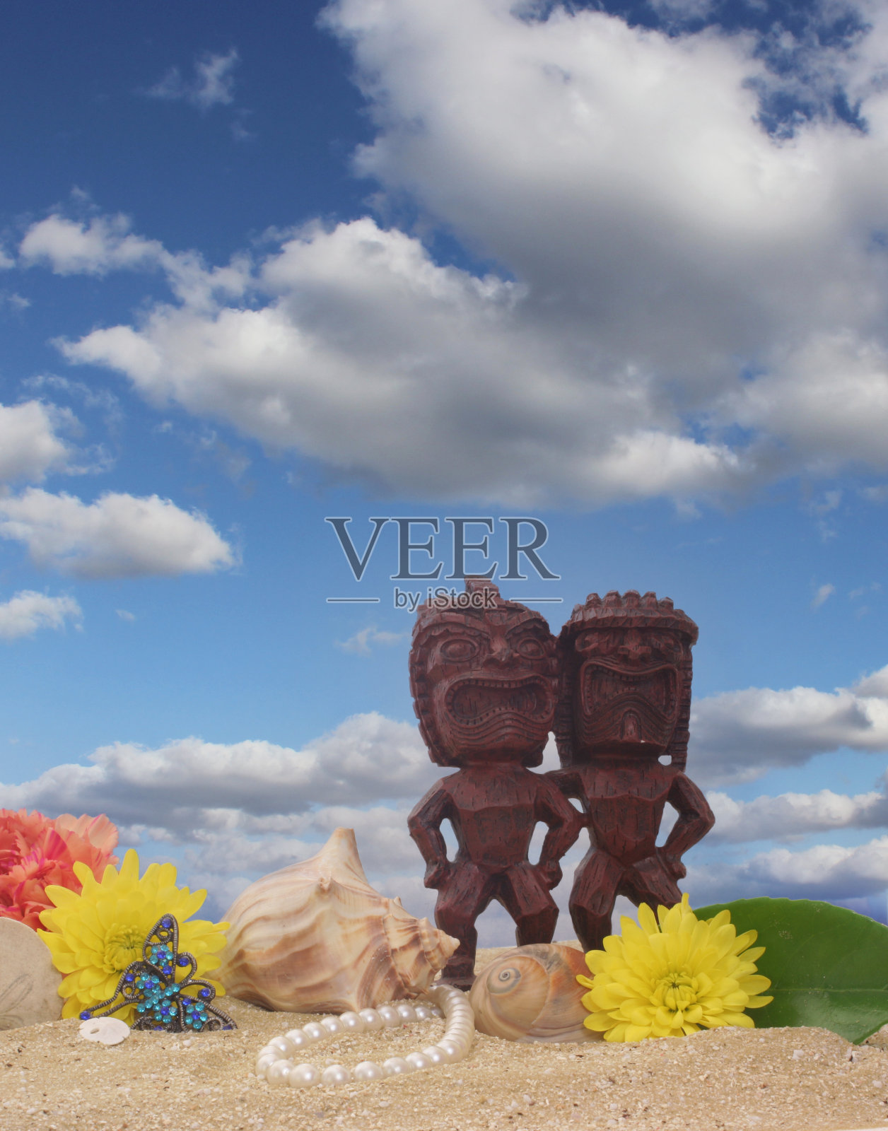 沙滩上的提基雕像，花和贝壳照片摄影图片