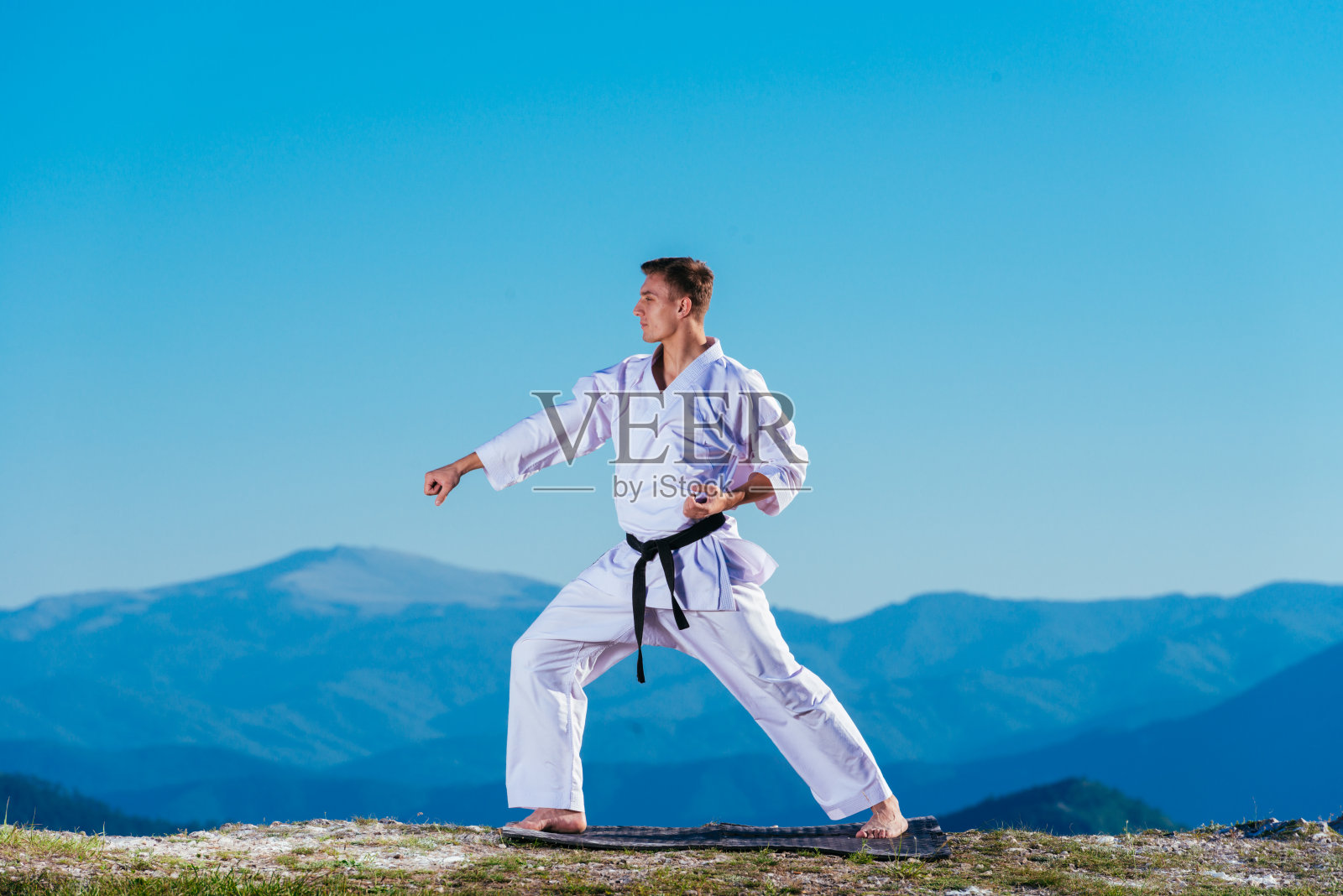 金发的空手道运动员在一个阳光明媚的日子，在山顶上表演一系列的踢腿、出拳和拦阻。照片摄影图片