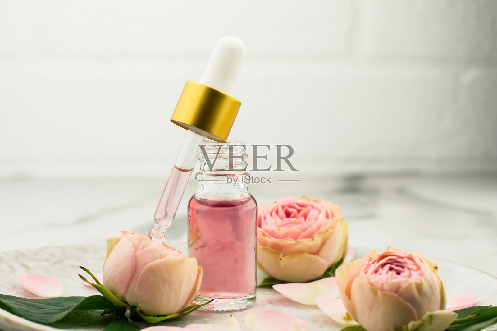 一个瓷盘上放着一瓶打开的玫瑰油和一个吸管，里面装满了用于面部皮肤再生和护理的化妆品。照片摄影图片