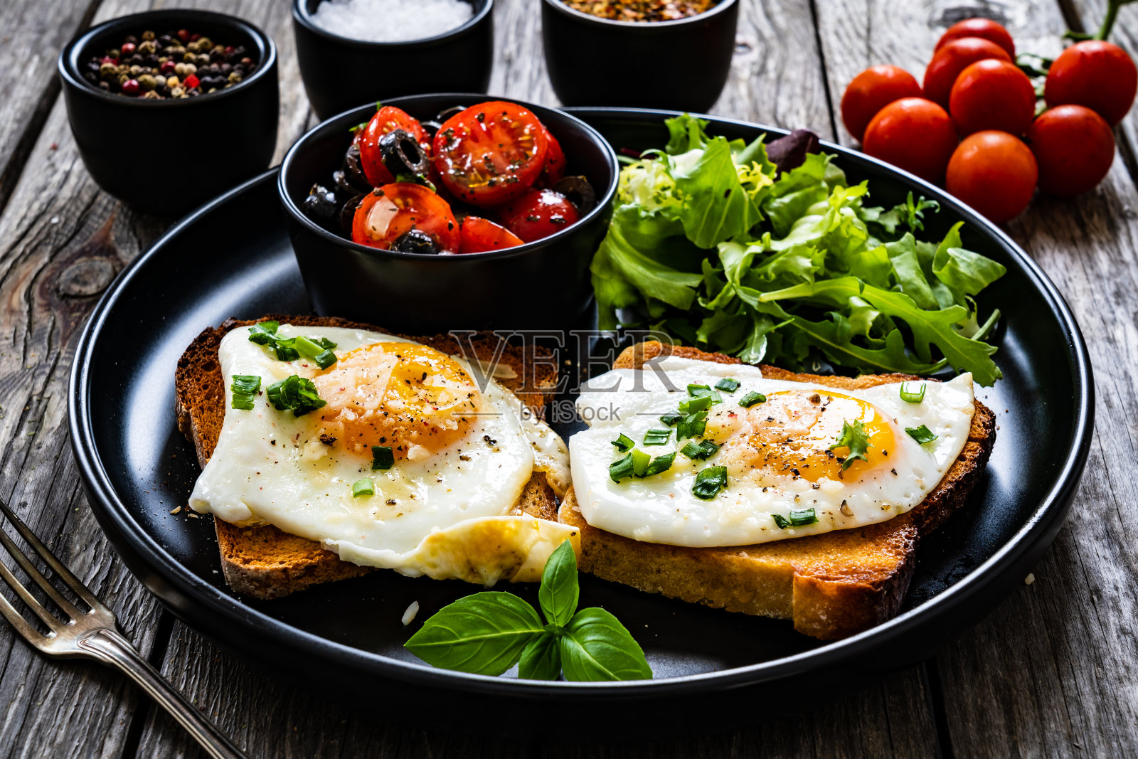 欧式早餐:烤面包配单面煎鸡蛋，木桌上放生菜和圣女果照片摄影图片