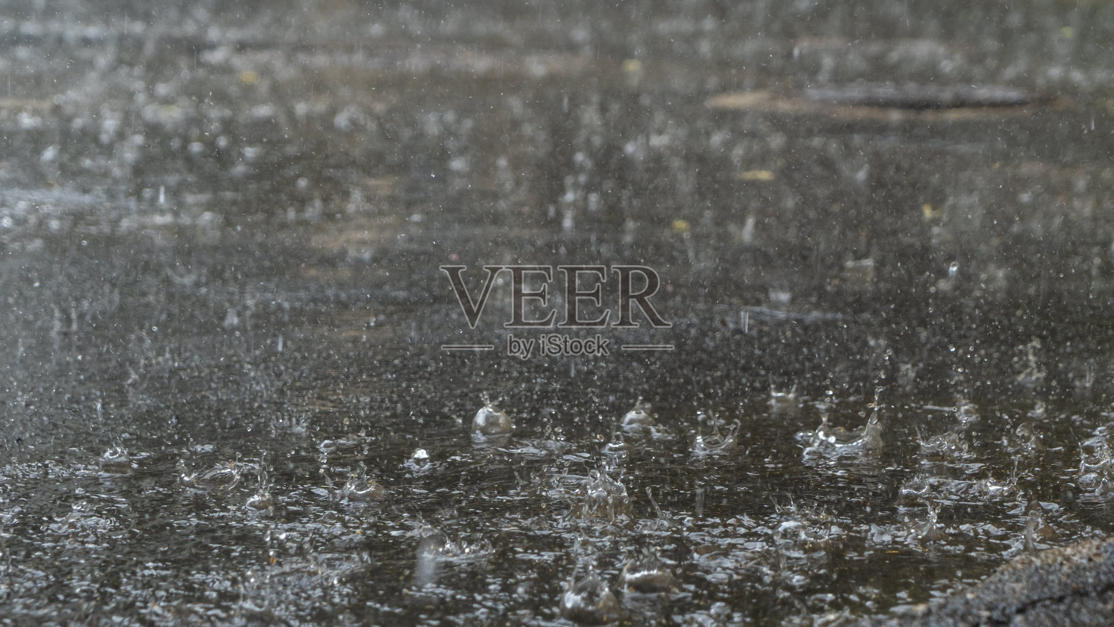 雨天雨滴打在水坑上。雨点落在城市沥青路面上的大水坑里。照片摄影图片