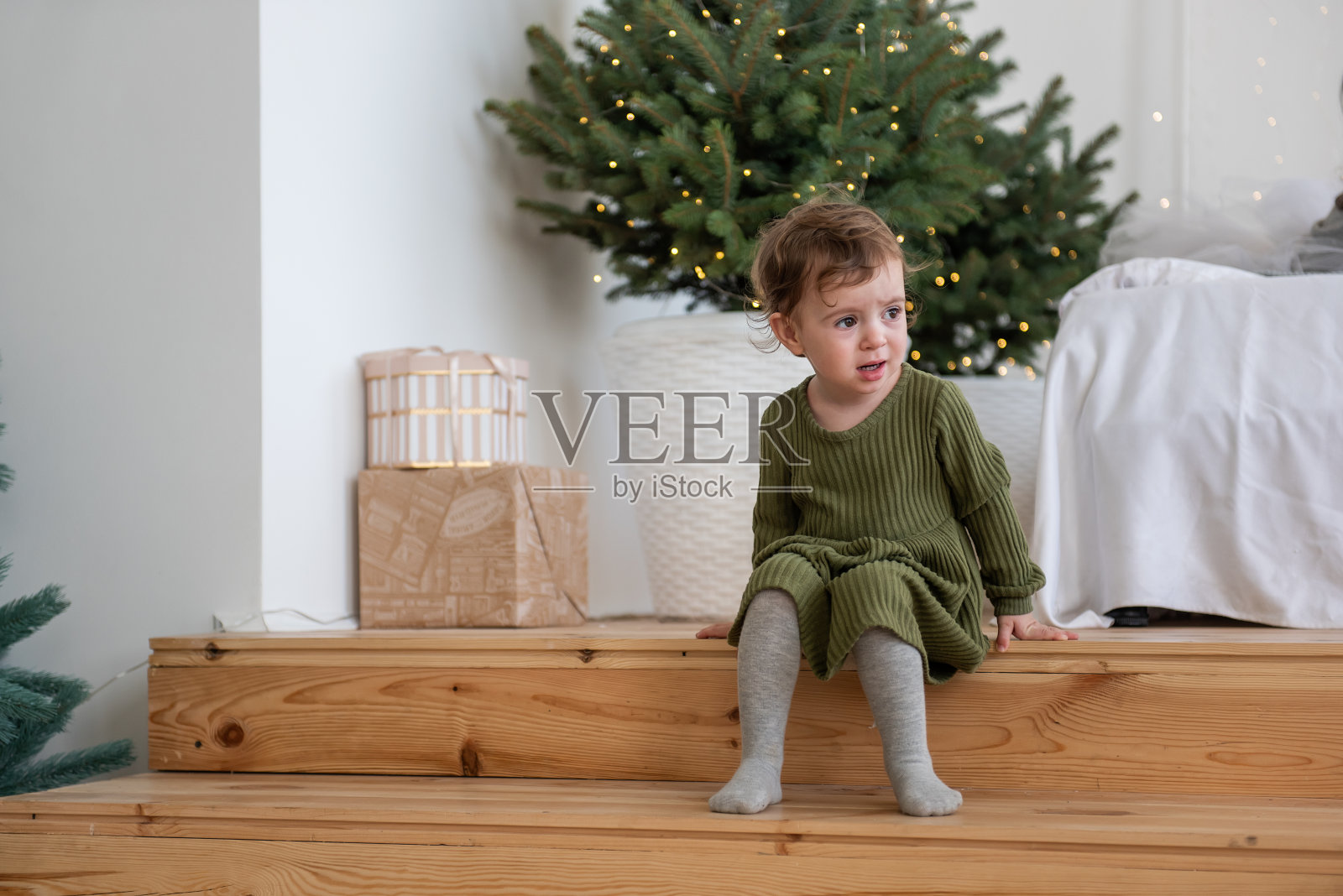 小女孩穿着温暖的绿色连衣裙坐在圣诞树旁的木台阶上，阁楼里有花环照片摄影图片