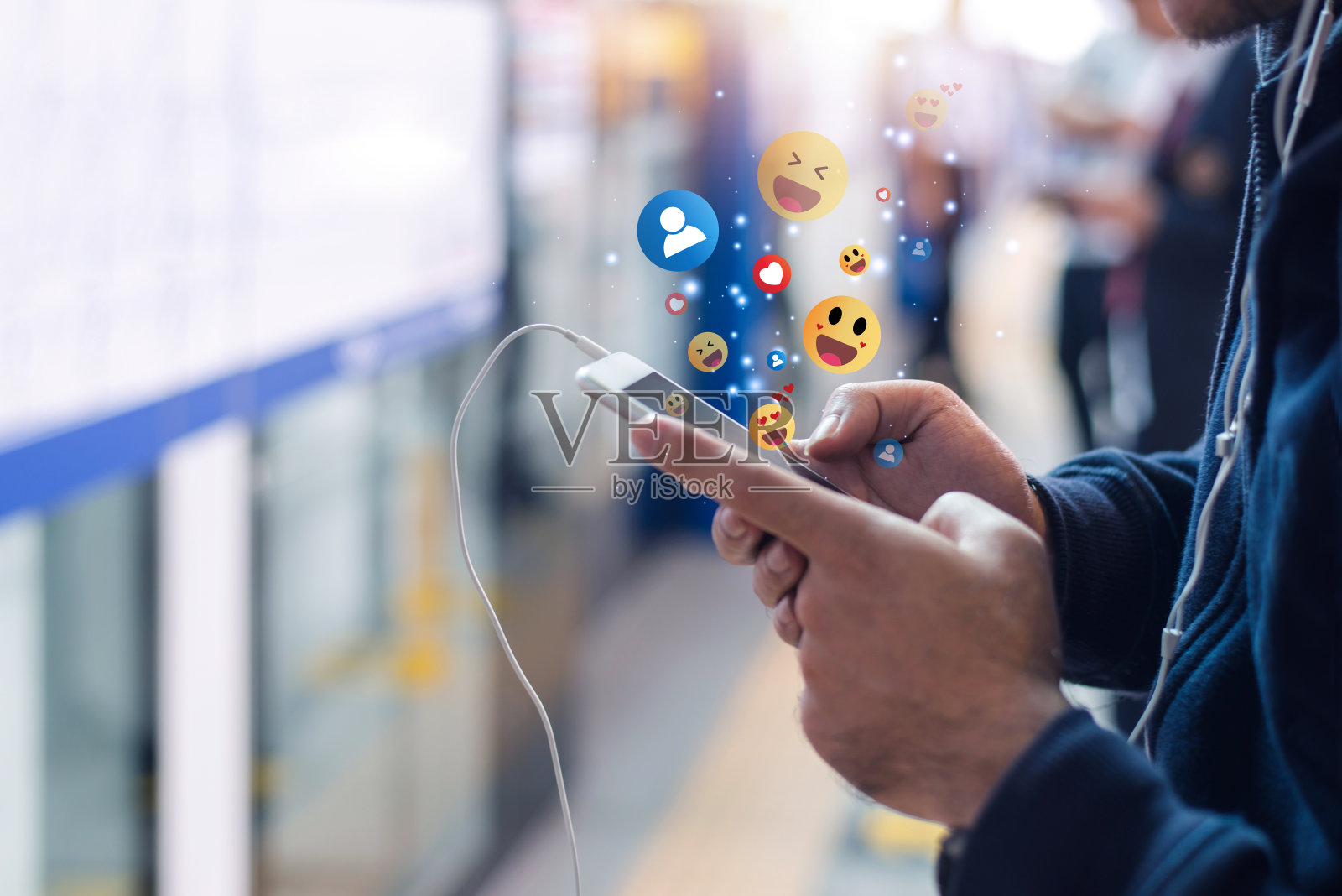 年轻的亚洲男子在火车站观看视频直播，通过表情符号和文字在线打字与他人交流。照片摄影图片