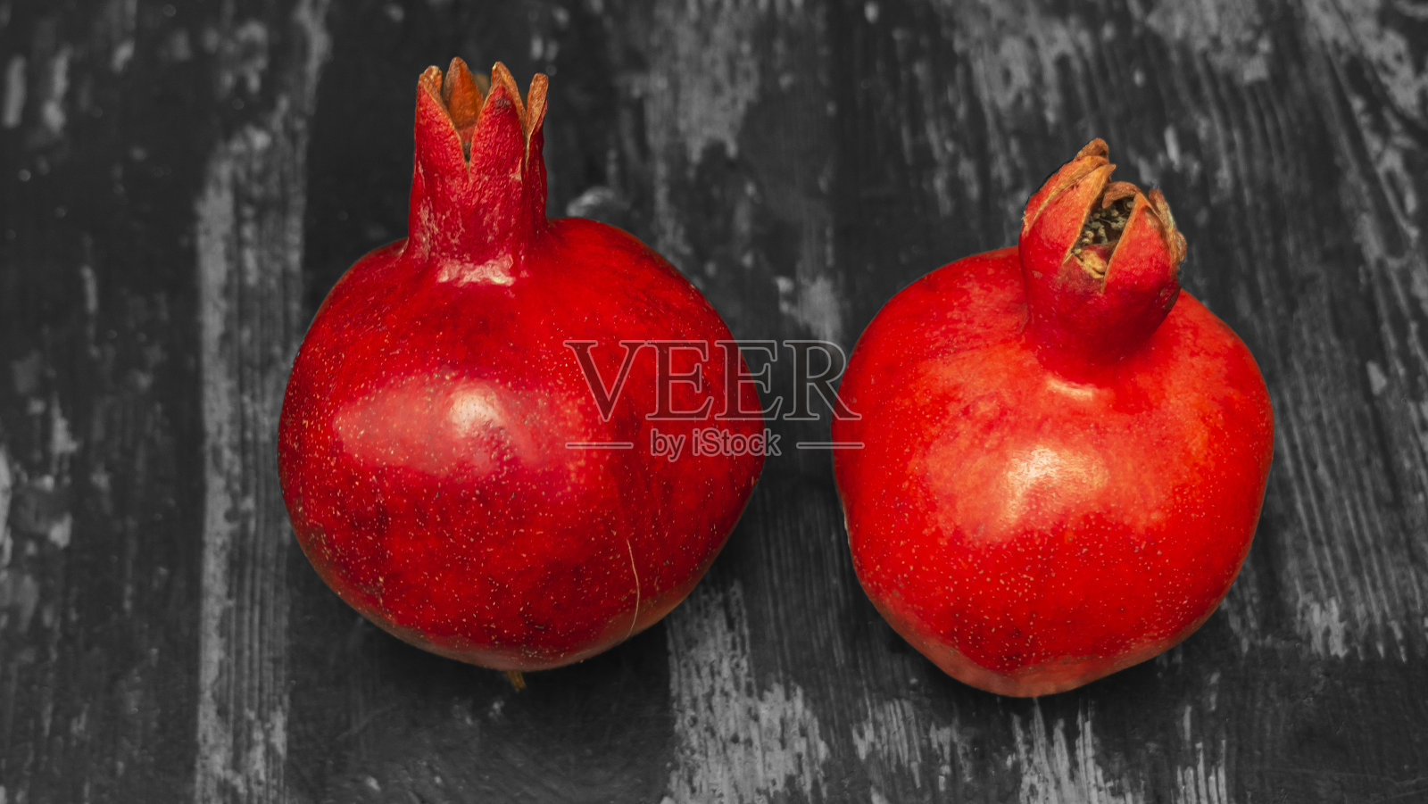 桌子上放着两个红石榴。两颗成熟的石榴石放在桌子上，背景是黑白木墙。照片摄影图片