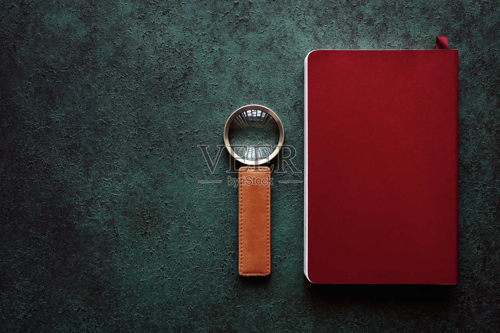 放大镜和关闭的书在红色封面上绿色纹理的背景照片摄影图片