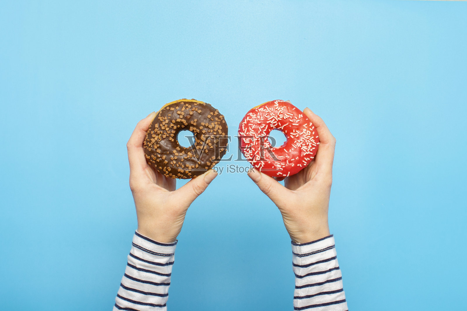 蓝色背景下，女性手拿着甜甜圈。概念糖果店，糕点，咖啡店。横幅。平铺，俯视图照片摄影图片