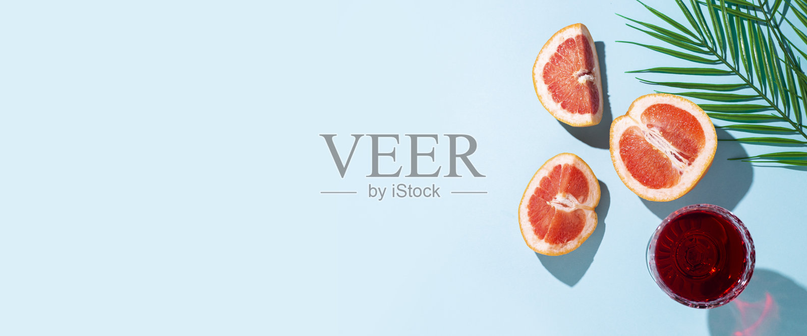 一杯红酒，在蓝色的背景上切柚子和棕榈叶。俯视图，平铺。横幅照片摄影图片