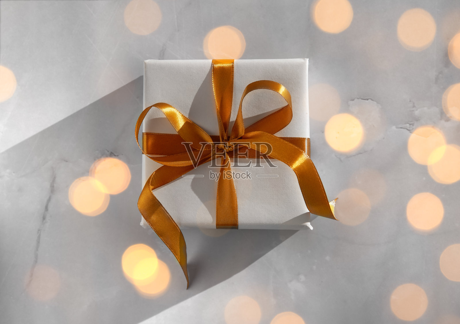 礼品盒包装在白色的纸与金色的蝴蝶结节日的灯光背景照片摄影图片
