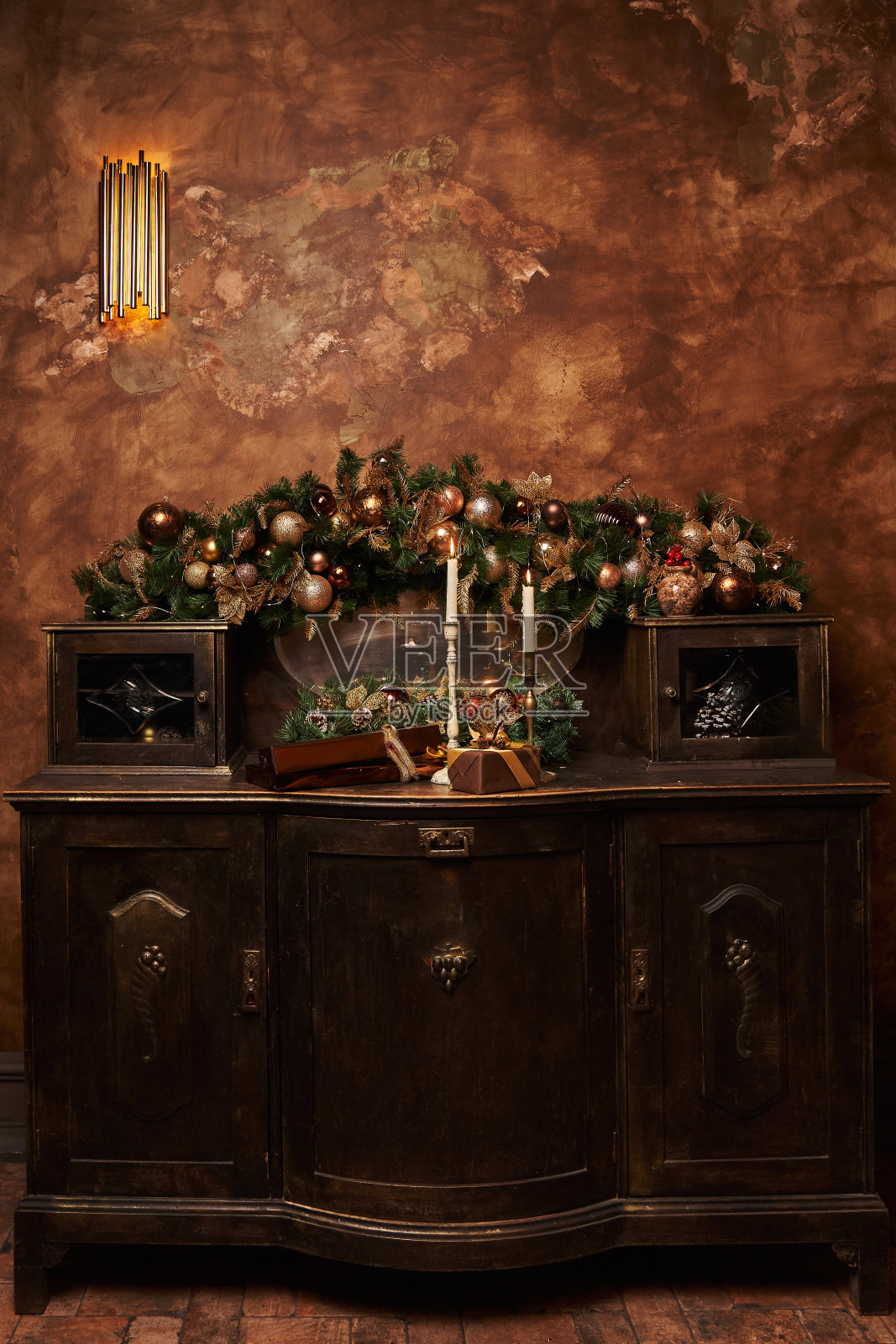 一个旧的五斗橱，上面点着蜡烛，背景是挂在云杉树枝上的亲属装饰物，旁边装饰着球和礼物。美丽的圣诞背景照片摄影图片
