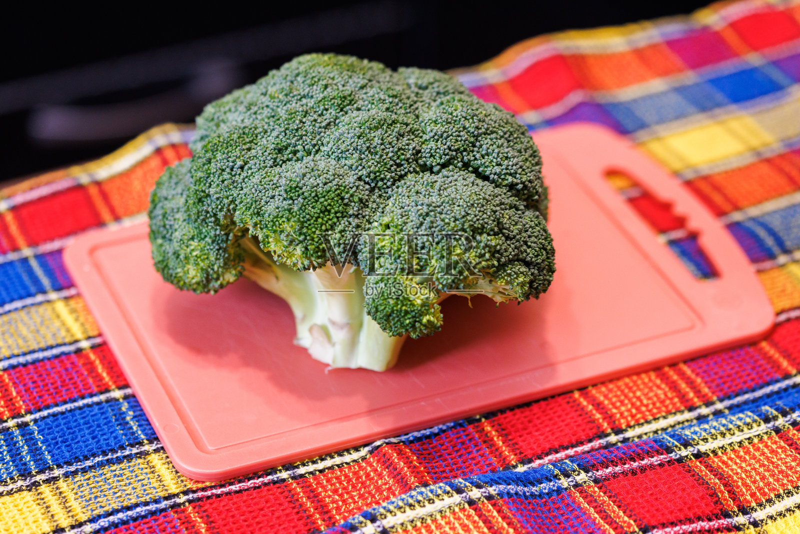 一个绿色的花椰菜头放在粉色的塑料切菜板上，下面是彩色的毛巾照片摄影图片