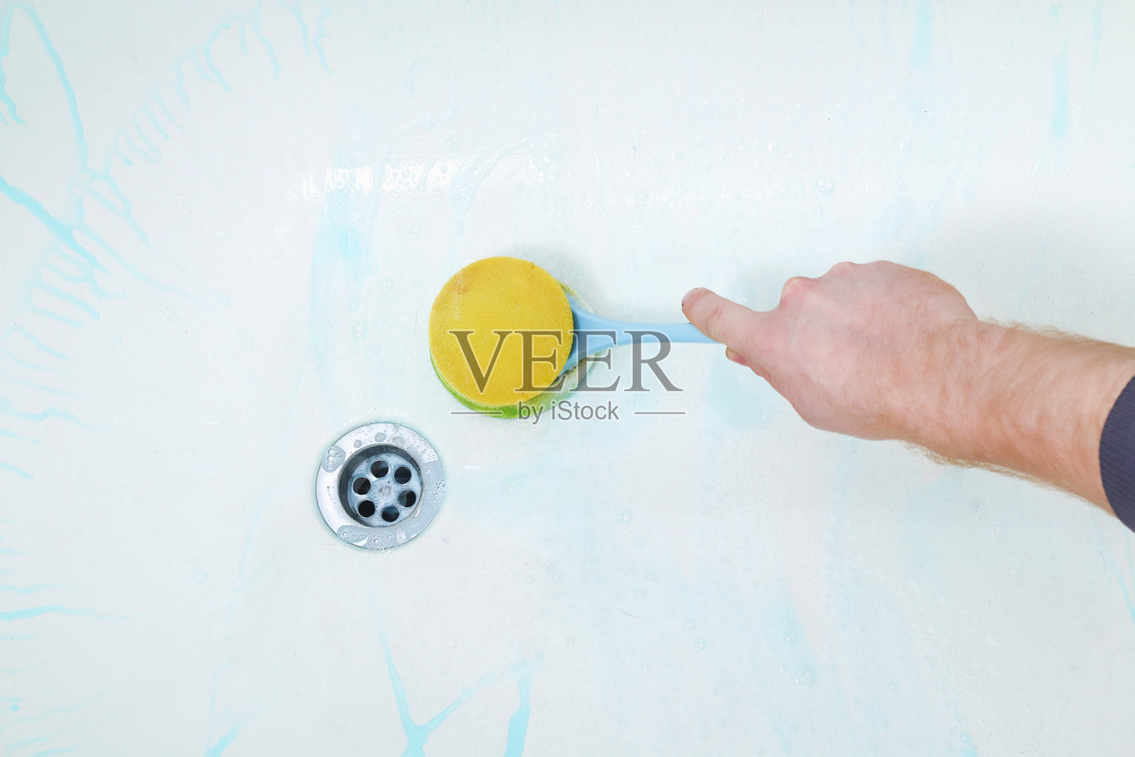 男人涂上沐浴清洁剂，用刷子、抹布擦洗沐浴。打扫浴室。照片摄影图片