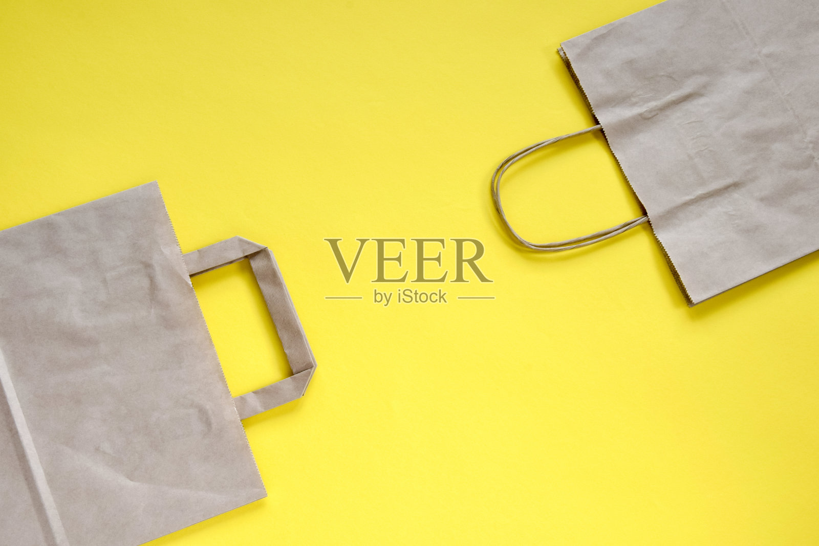 回收牛皮纸购物袋与处理，孤立在黄色背景，平躺，模型。两个折叠的空纸袋。对角线的安排。特写镜头。有选择性的重点。副本的空间。照片摄影图片