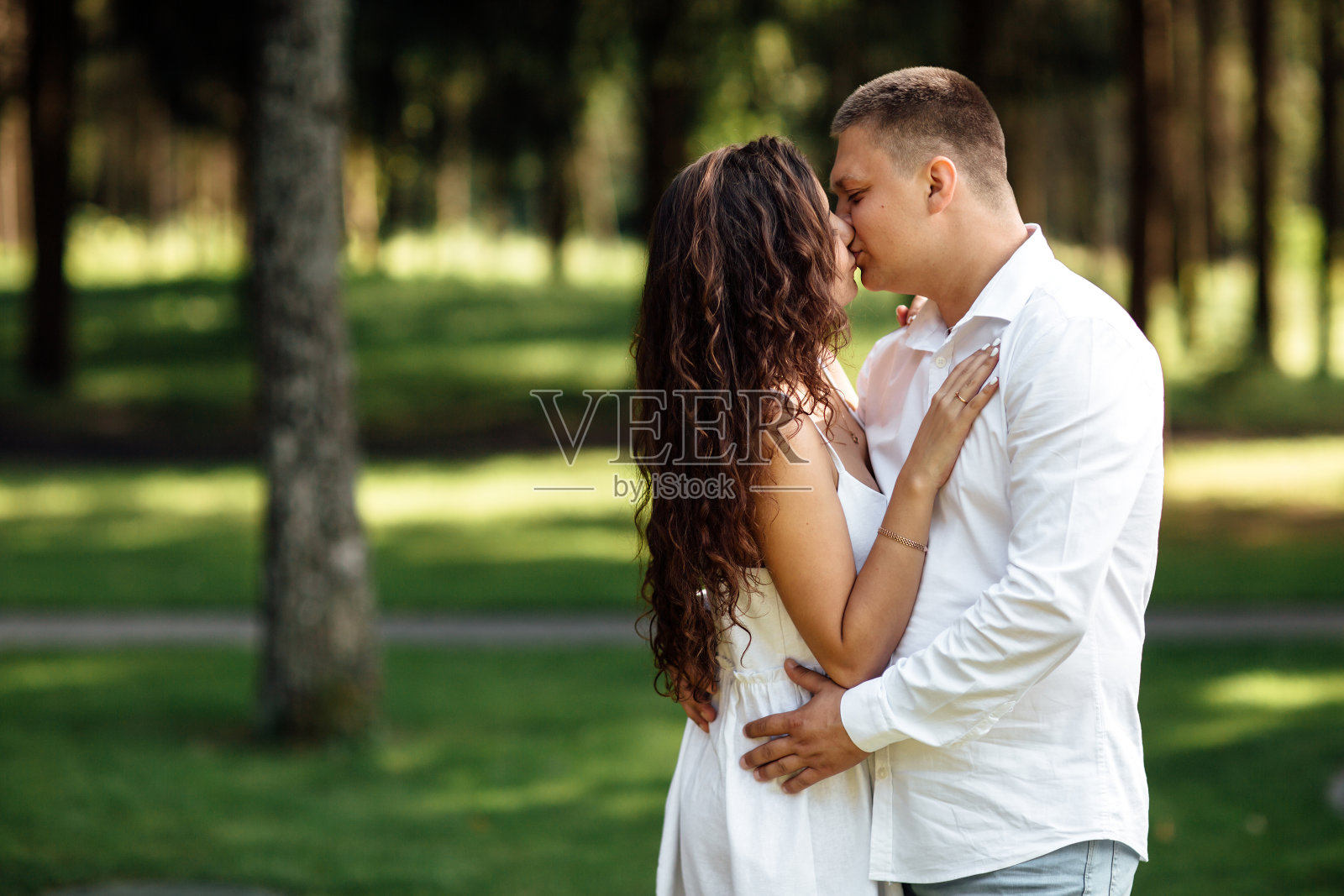 夏日里，一对相爱的年轻情侣在公园里接吻。男人和女人在户外拥抱照片摄影图片
