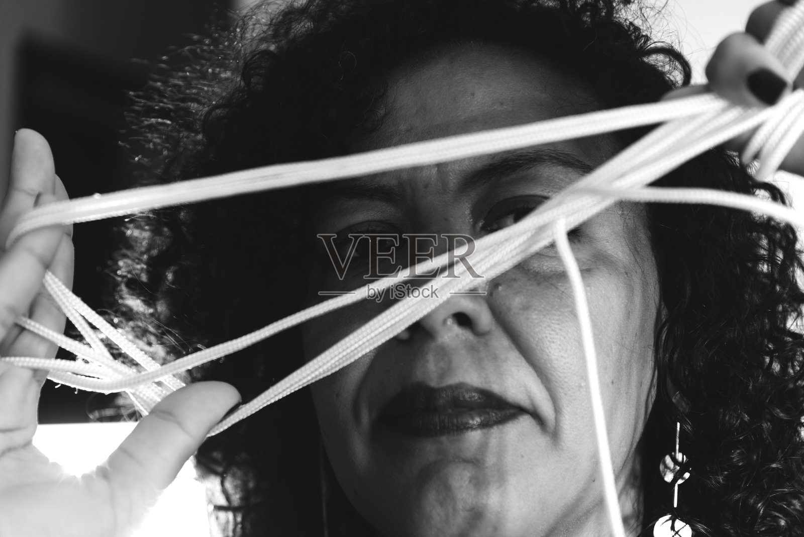 一个女人的脸的特写穿着彩色的裙子，在浅灰色的背景下，手拉着绳子。照片摄影图片