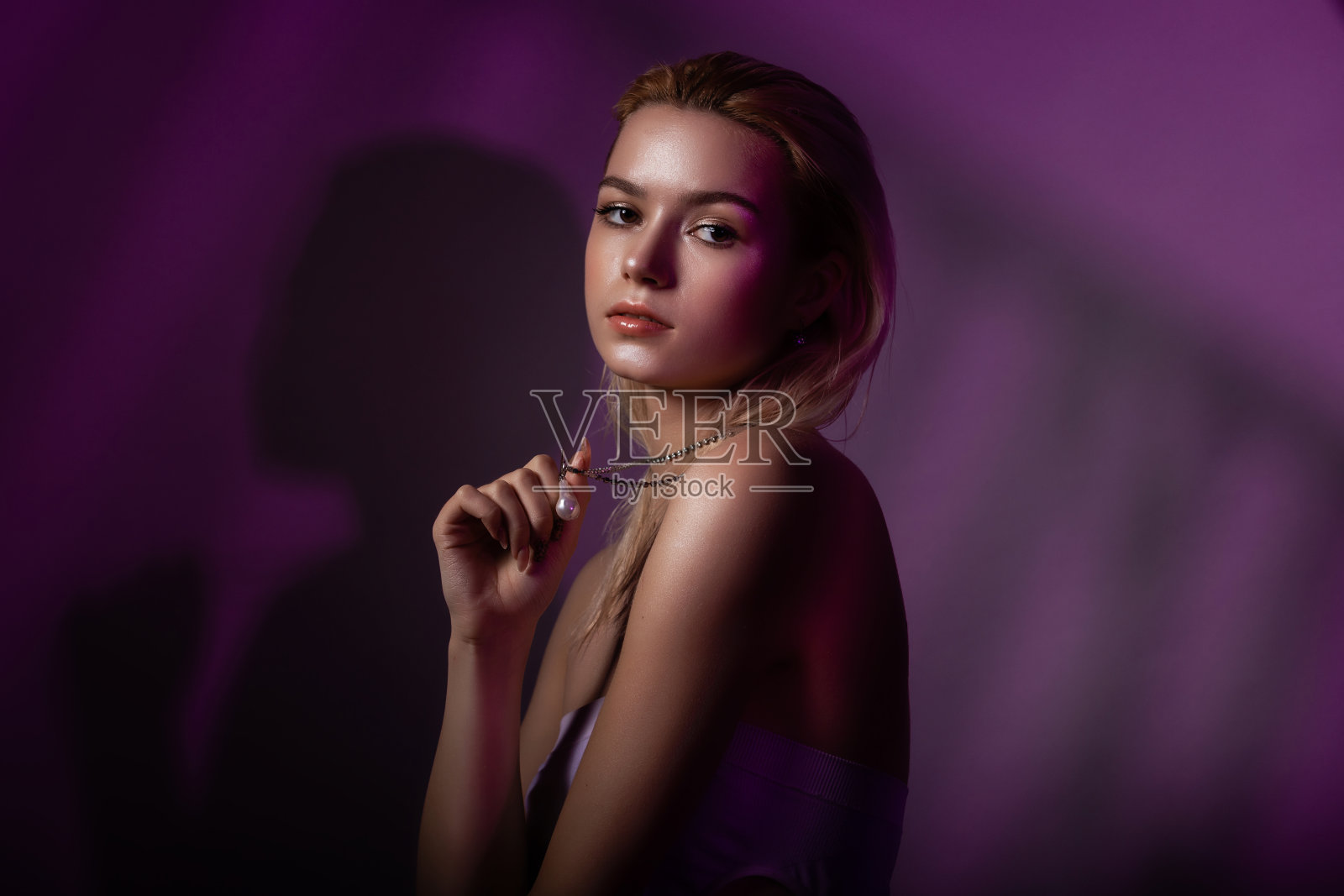 高级时装模特的脸在彩色明亮的霓虹灯紫色。美丽的女人在工作室摆姿势，并持有或显示一个链，发光闪闪明亮的霓虹灯妆。照片摄影图片