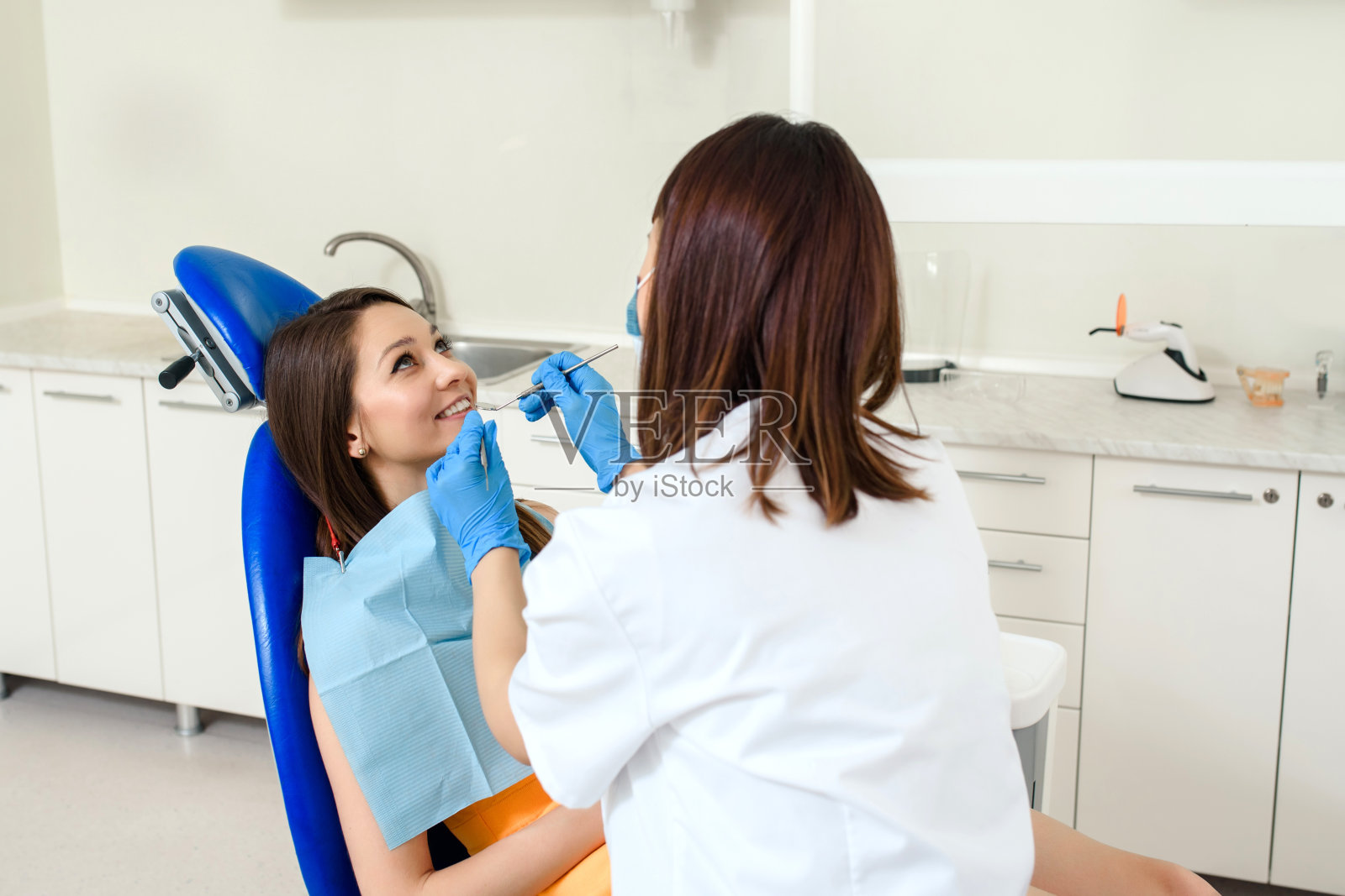 牙科医生在诊所用牙科器械检查病人的牙齿。照片摄影图片