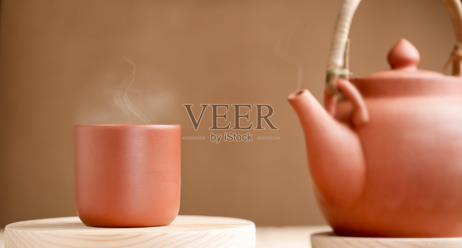 陶瓷陶瓷杯与热蒸汽和茶壶在质朴的木制桌子，棕色的背景照片摄影图片
