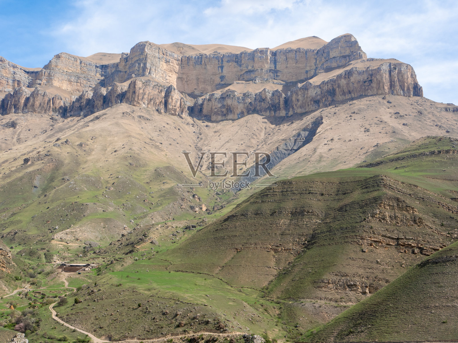 在蓝天和绿草如茵的背景下，你可以看到巍峨的岩石山脉环绕着Gizhgit湖。俄罗斯，高加索，厄尔布鲁斯地区。照片摄影图片