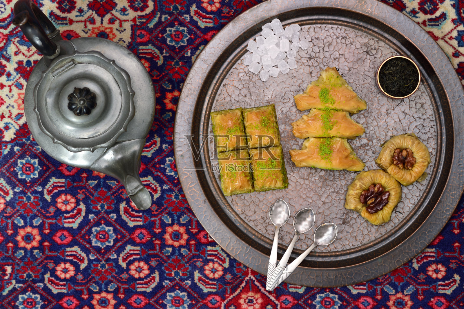 新鲜的果仁蜜饼，一种由酥皮点心和坚果制成的东方糕点，放在铜托盘上，旁边是一个古老的东方地毯上的旧茶壶，从上面拍摄照片摄影图片
