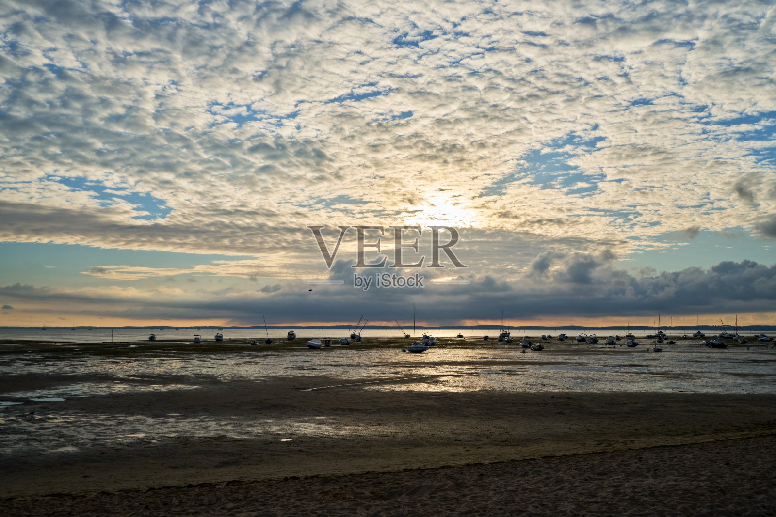 傍晚，小帆船在低潮时躺在沙滩上，前面是多云的蓝天照片摄影图片