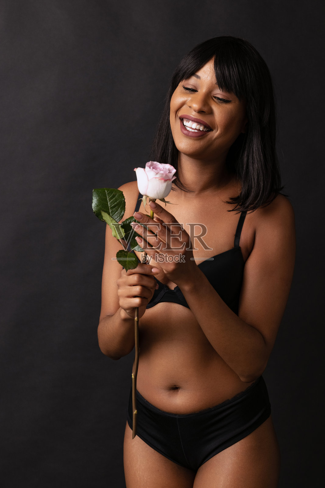漂亮微笑的深色皮肤女孩的肖像在黑色内衣与花孤立在黑暗的工作室背景。自然美景的概念。照片摄影图片