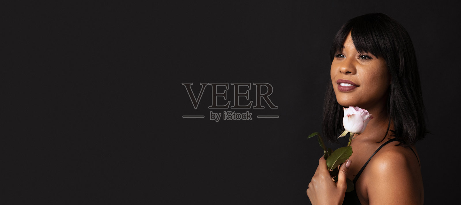 特写漂亮的深色皮肤的女孩在黑色内衣与花孤立在黑暗的工作室背景。自然美景的概念。照片摄影图片