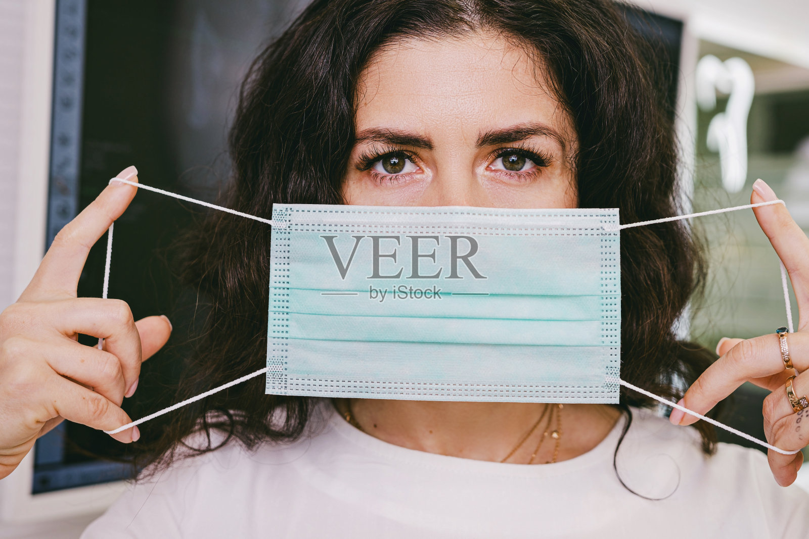 近距离的照片，一个深色头发的女人看着相机用医用口罩遮住她的脸在她的手中。照片摄影图片